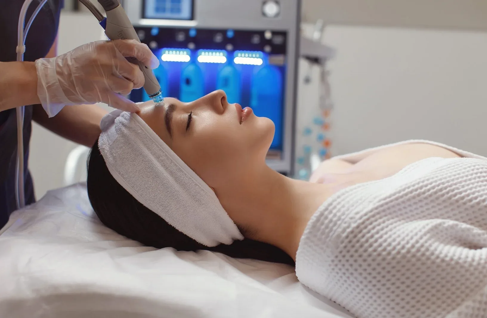 Especialista aplicando un tratamiento facial a una clienta recostada en la camilla del estudio.
